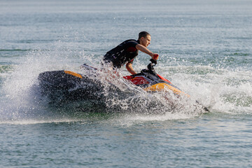 Fototapeta premium Young man rides a jet ski across turquoise waters during seaside vacation. Concept water sports passion and active leisure