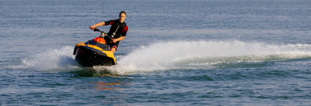 Young man speeds on a jet ski under the bright summer sun. Concept freedom, adrenaline, and water thrill