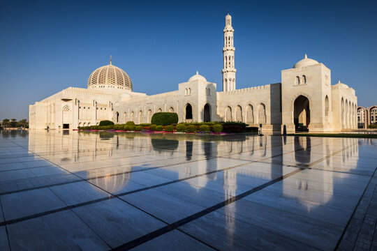 View of the Sultan Qaboos Grand Mosque's intricate details shimmer and reflect on the polished stone, contrasting with the clear blue Omani sky, Muscat, Muscat Governorate, Oman.