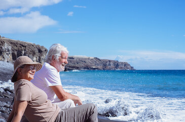 Relaxed senior couple in peaceful vacation sitting on the seashore while waves splashing on the...