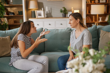 A teenage girl is passionately discussing her problems with her mother on a sofa in a warm living...