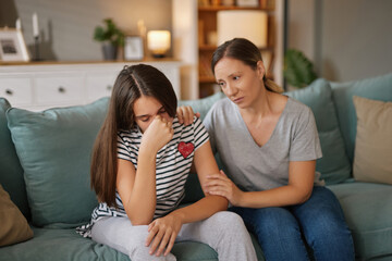 Two individuals are seated on a couch, with a teenager visibly upset while an adult offers comfort...
