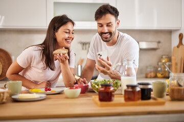 A couple shares a joyful breakfast experience in their modern kitchen while both looking at a...