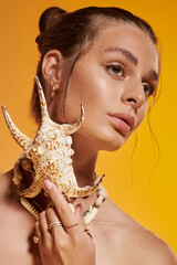 Young woman showcases summer fashion with seashell necklace in vibrant studio setting