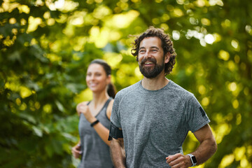 Two enthusiastic runners smile while jogging on a tree-lined path, embracing a healthy lifestyle in...