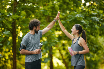 Two active individuals share a joyful moment in a park, giving each other high fives after a...