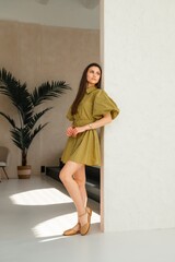 A woman wearing a stylish green dress is leaning against a wall in a room