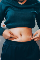 woman's hand holding excessive belly fat, overweight concept