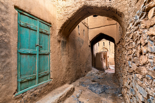 View of weathered turquoise doors and an arched tunnel carved from earth tones create an inviting scene into an old alleyway, al hamra, Oman.