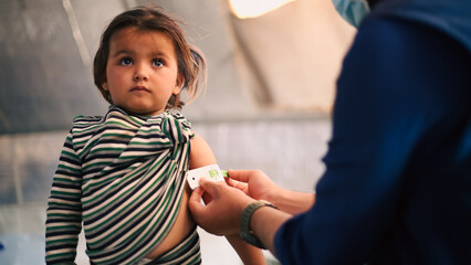 A doctor examines children's malnutrition inside a refugee camp. Malnutrition was measured using a mid-upper arm circumference belt.