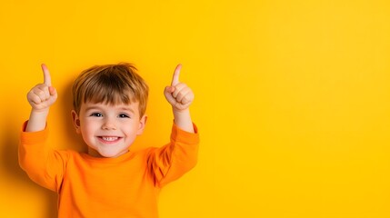 Smiling child lying on yellow background pointing upwards with both hands.