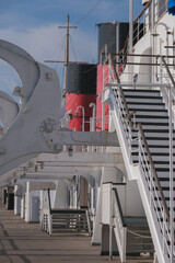 Red and black funnel of historic oceanliner ocean liner Mary against deep blue sky with clouds	