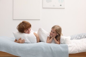 Cute children with pillows lying on bed at home