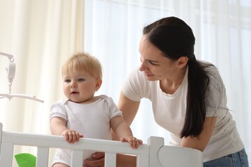 Mother playing with her cute baby in crib at home