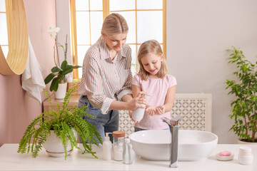 Happy mother and daughter washing their hands in bathroom
