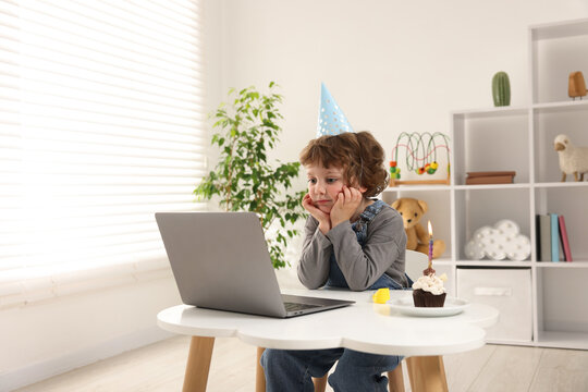 Birthday celebration. Little boy with cupcake having video call via laptop at table indoors - Powered by Adobe