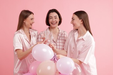 Pajama party. Happy friends with balloons clinking glasses on pink background