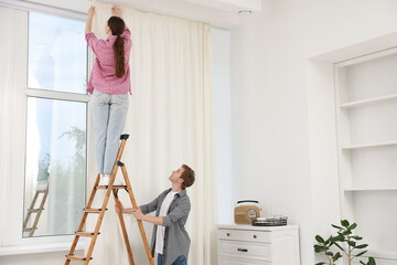 Couple putting up curtains using ladder in room © New Africa