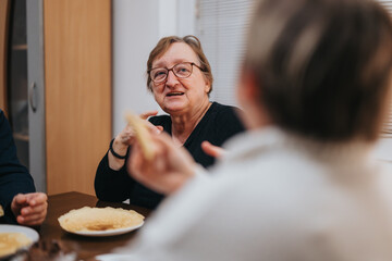 A relaxed elderly woman in conversation over a meal, sharing happy moments in a home setting with family and friends, showcasing warmth and connectedness.