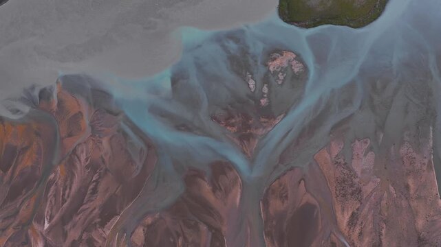 Aerial view of vibrant braided rivers with turquoise channels flowing through reddish brown terrain. Smooth camera motion highlights intricate patterns.