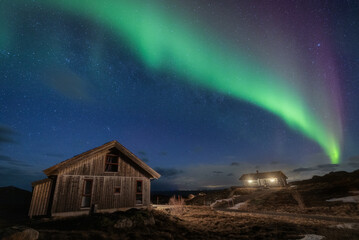 Lofoten Islands, Norway - 15 March 2023: View of ethereal green and purple aurora borealis dancing above rustic cabins in the tranquil, starlit Nordic night.