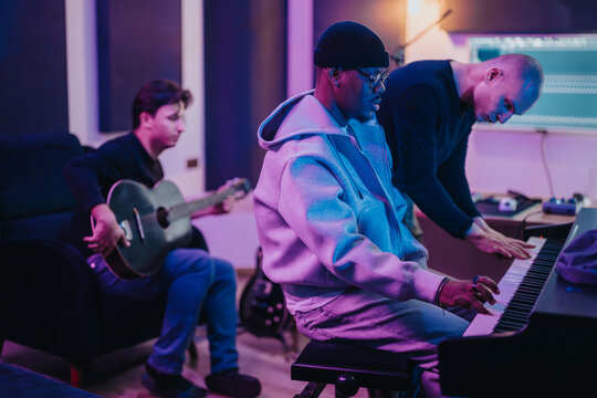A group of diverse musicians working together in a recording studio, playing guitar and piano. The scene captures creativity and collaboration among artists immersed in their music-making process. - Powered by Adobe