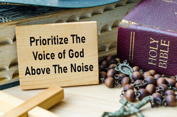 Prioritize The Voice of God Above The Noise text on wooden block with Holy Bible and Holy Rosary...