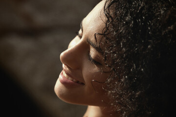 
A close-up of a woman with voluminous curly hair and a white pearl-embellished bikini top, smiling...