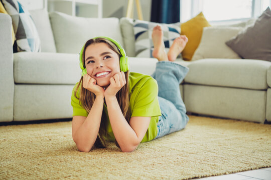Young woman enjoys relaxation indoors wearing headphones while lying comfortably on a cozy carpet in a modern living room