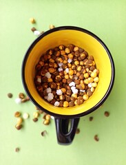 Vibrant roasted chickpeas, chana with sugar crystals in a bright yellow mug, isolated on a fresh...