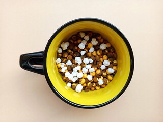 Vibrant roasted chickpeas, chana with sugar crystals in a bright yellow mug, isolated on a fresh...