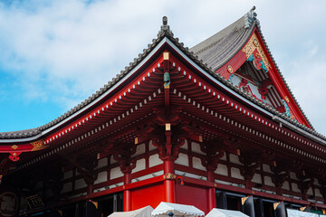 Fototapeta premium Close-up of a traditional Japanese temple roof with intricate red and white details against a blue sky with clouds.