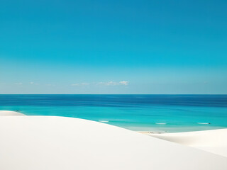 Obraz premium Serene view of white sand dunes meeting turquoise ocean under clear blue sky, evoking tranquility and natural beauty
