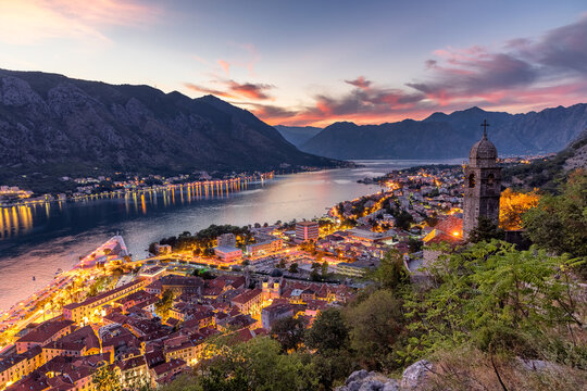 Aerial view of the Bay of Kotor, where the serene waters reflect the dusky sky, and city lights twinkle against the backdrop of majestic mountains, Kotor, Montenegro.