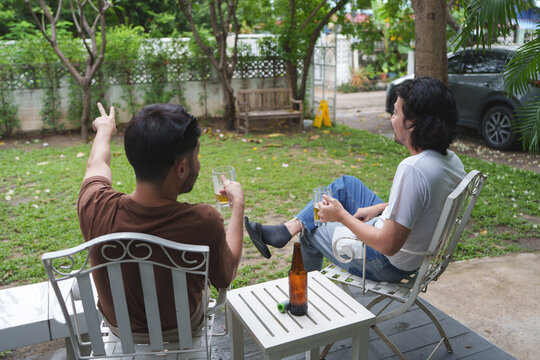 Asian male friends enjoying drinks on a patio, gesturing and talking in a private garden setting