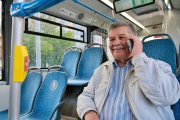 An elderly man uses a smartphone on public transportation. A pensioner on a bus
