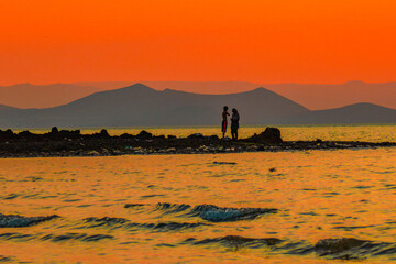 Scenic view of a man and a woman having fun at the beach against a golden sunset at Lake Turkana in Loiyangalani District, Kenya 