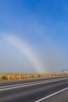 half a fogbow mistbow shining in light mist over rural paddock in farmland