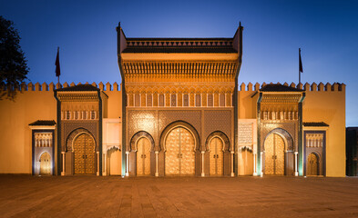 View of the grand, ornate gates illuminated against the dusky sky, revealing intricate tilework and golden doors, inviting exploration and wonder, Fes, Fez-MeknÃ¨s, Morocco.