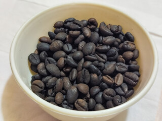 A bowl of freshly roasted coffee beans is dark in color, on a white background.