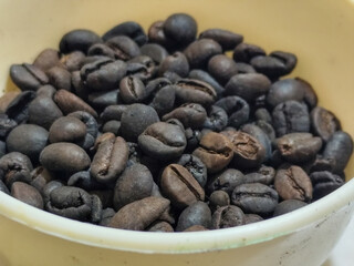 A bowl of freshly roasted coffee beans is dark in color, on a white background.