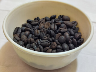 A bowl of freshly roasted coffee beans is dark in color, on a white background.