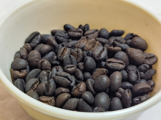 A bowl of freshly roasted coffee beans is dark in color, on a white background.