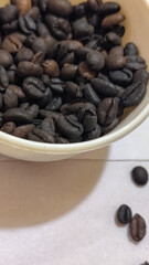 A bowl of freshly roasted coffee beans is dark in color, on a white background.