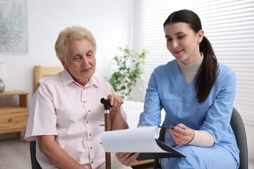 Fototapeta premium Nurse with clipboard examining senior woman indoors. Home health care service