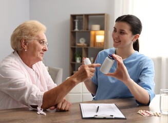 Nurse giving pills to senior woman at wooden table indoors. Home health care service