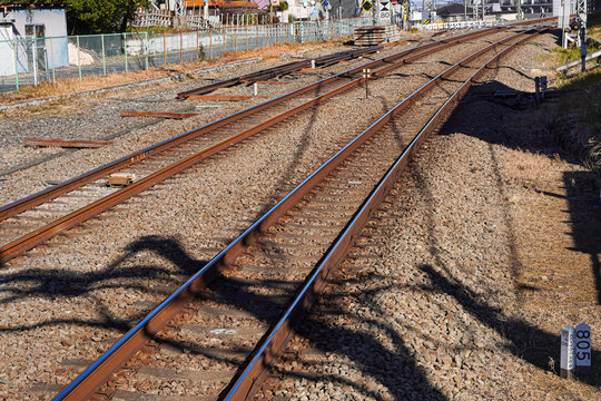 Parallel train tracks extend through a landscape, with shadows cast by trees.