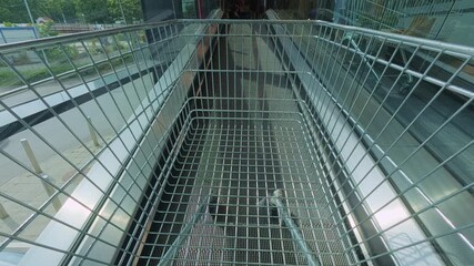 Empty shopping cart moving on an inclined travelator inside a modern mall or supermarket, heading toward the entrance or parking area - Powered by Adobe