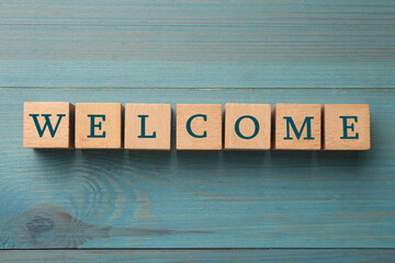 Word Welcome made of wooden cubes on light blue table, top view