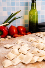 Fresh ravioli with flour on wooden cutting board with vegetables and spices. Vertical Orientation